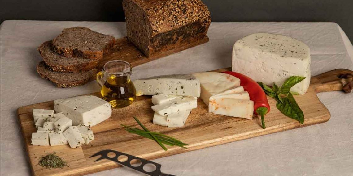 Variedade de queijos artesanais chilenos com ervas e malagueta, acompanhados de pão integral e azeite numa tábua.
