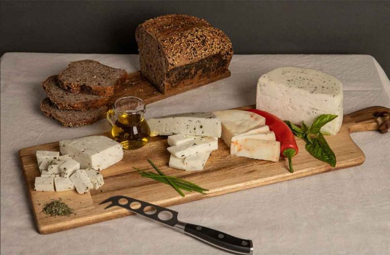 Variedade de queijos artesanais chilenos com ervas e malagueta, acompanhados de pão integral e azeite numa tábua.