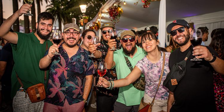 Young people toasting with red and white wine at a lively grape harvest festival in Chile, celebrating the 2026 harvest outdoors at sunset.