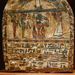 Ancient Egyptian coffin lid with hieroglyphic inscriptions and a winged figure motif above a scene of people.